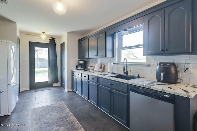 kitchen with a sink, baseboards, backsplash, freestanding refrigerator, and dishwasher