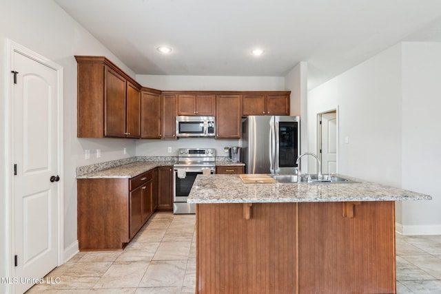 kitchen featuring sink, stainless steel appliances, light stone counters, kitchen peninsula, and a kitchen bar