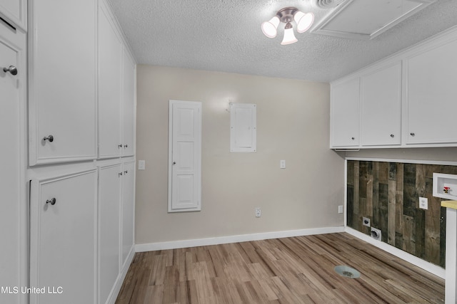 laundry area with electric panel, light hardwood / wood-style flooring, a textured ceiling, and cabinets