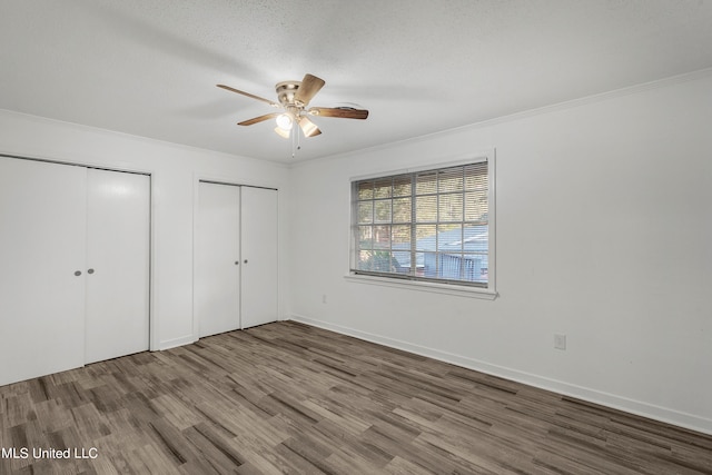 unfurnished bedroom featuring ceiling fan, hardwood / wood-style flooring, multiple closets, and ornamental molding