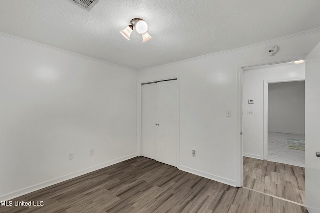 unfurnished bedroom with ornamental molding, a closet, a textured ceiling, and wood-type flooring