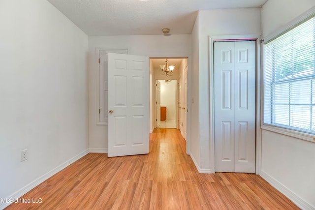 unfurnished bedroom with a closet, a textured ceiling, a chandelier, and light wood-type flooring