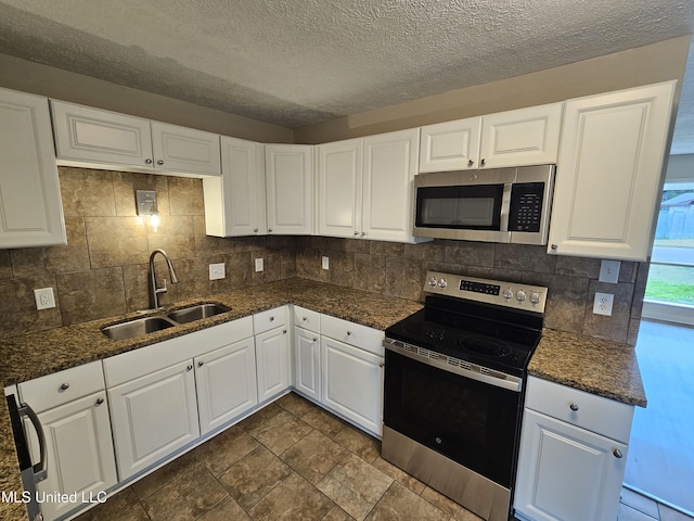 kitchen featuring dark stone countertops, a sink, stainless steel appliances, white cabinetry, and tasteful backsplash