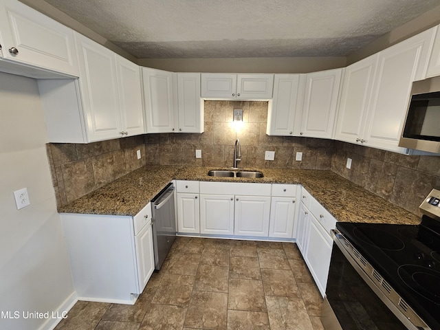 kitchen with tasteful backsplash, dark stone countertops, appliances with stainless steel finishes, white cabinets, and a sink