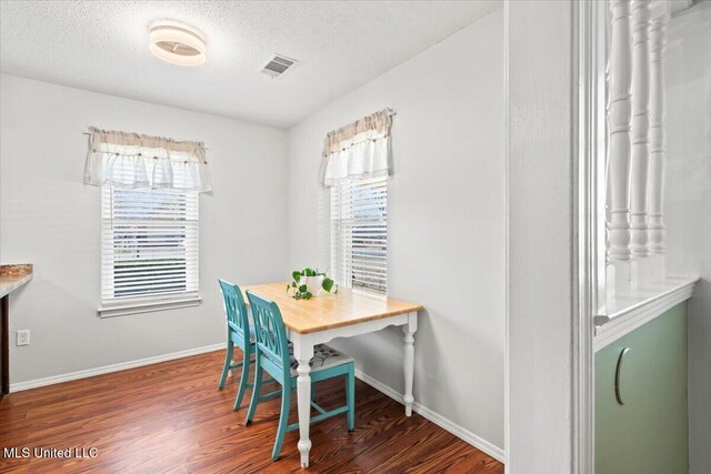 dining space with baseboards, wood finished floors, visible vents, and a textured ceiling