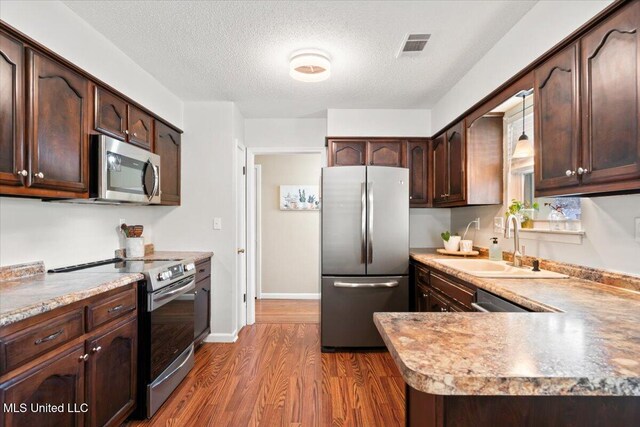 kitchen featuring visible vents, dark wood-type flooring, a sink, stainless steel appliances, and dark brown cabinetry