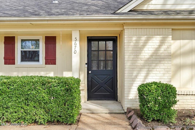 entrance to property with brick siding and a shingled roof