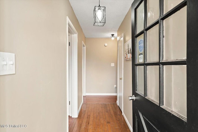 hall featuring baseboards, a textured ceiling, and wood finished floors