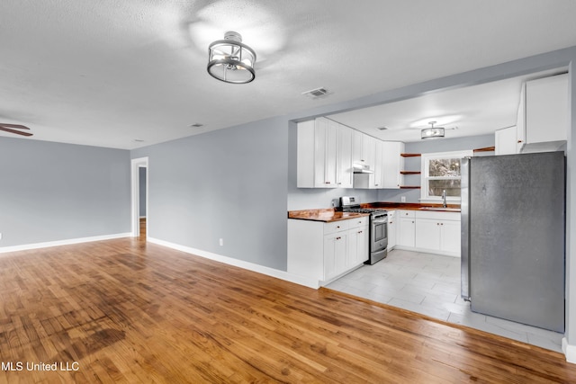 kitchen featuring light wood-style flooring, appliances with stainless steel finishes, open floor plan, white cabinetry, and open shelves