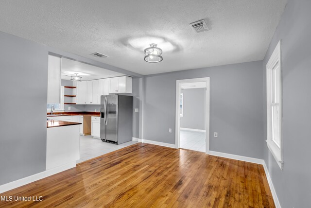 kitchen with stainless steel fridge, visible vents, white cabinets, dark countertops, and open shelves