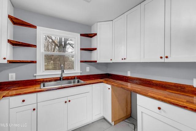 kitchen with open shelves, marble finish floor, wooden counters, and a sink