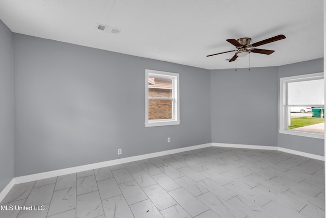 spare room with marble finish floor, visible vents, plenty of natural light, and baseboards