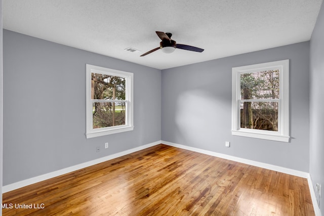 unfurnished room featuring a healthy amount of sunlight, visible vents, baseboards, and wood finished floors