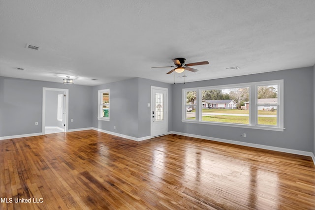 unfurnished living room featuring light wood-type flooring, visible vents, baseboards, and a textured ceiling