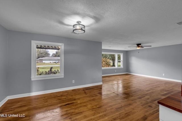 empty room with a textured ceiling, ceiling fan, wood finished floors, and baseboards