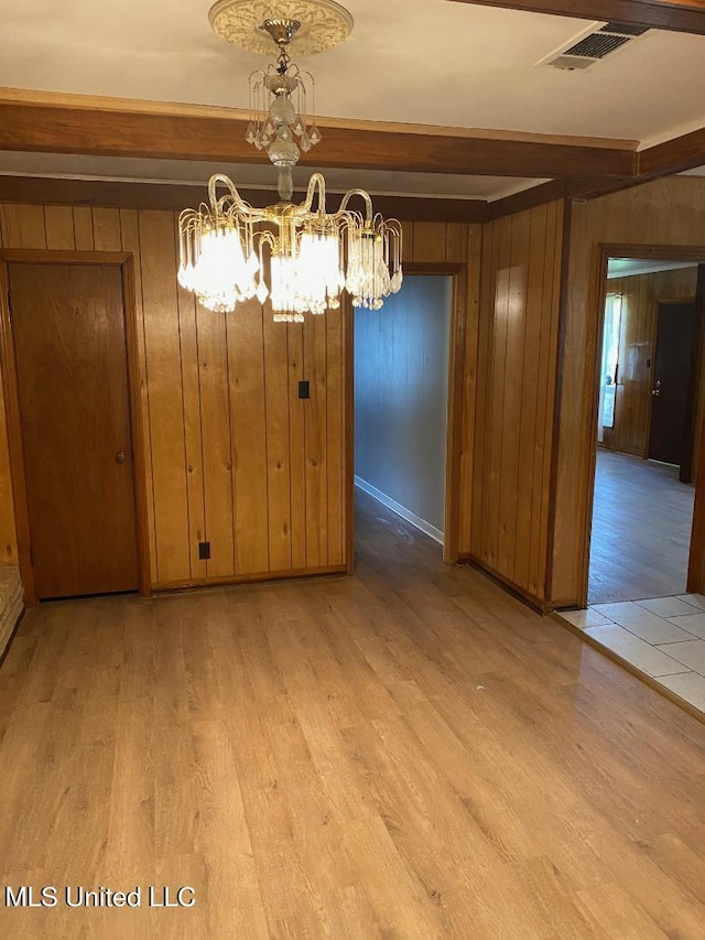 unfurnished dining area featuring beam ceiling, a chandelier, wooden walls, and light hardwood / wood-style floors