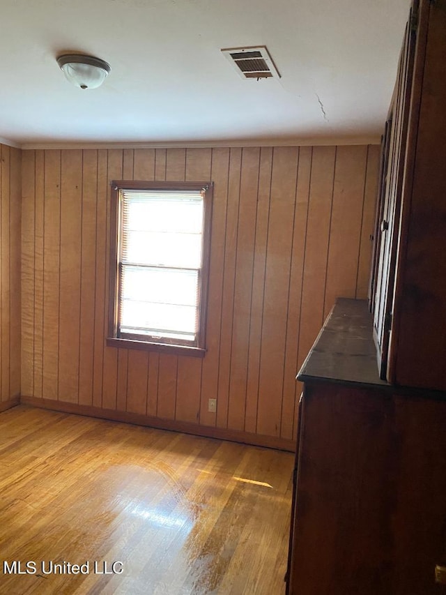 unfurnished room with light hardwood / wood-style floors and wooden walls