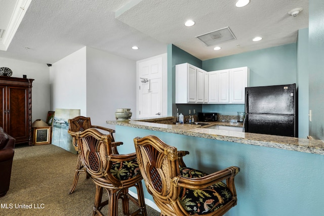 kitchen with black refrigerator, a textured ceiling, white cabinetry, and dark carpet