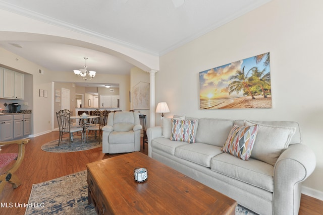 living room with ornate columns, an inviting chandelier, ornamental molding, and hardwood / wood-style flooring