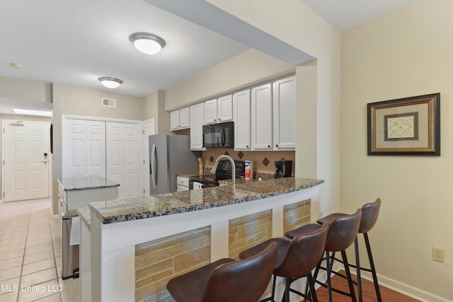 kitchen with kitchen peninsula, a kitchen bar, stainless steel appliances, dark stone countertops, and white cabinets