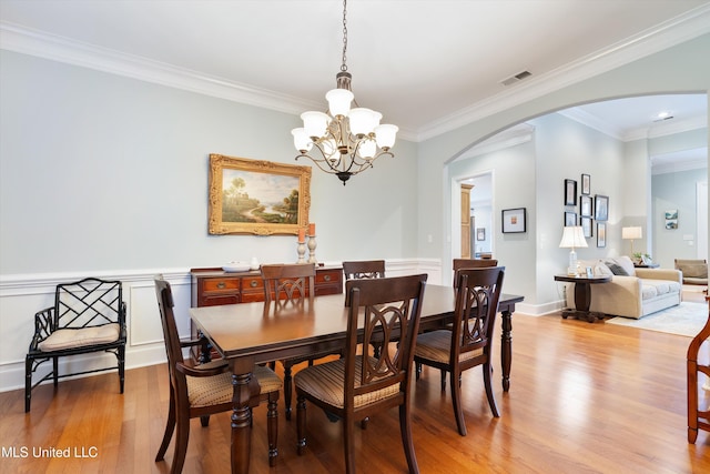 dining area with arched walkways, light wood-style flooring, visible vents, ornamental molding, and an inviting chandelier