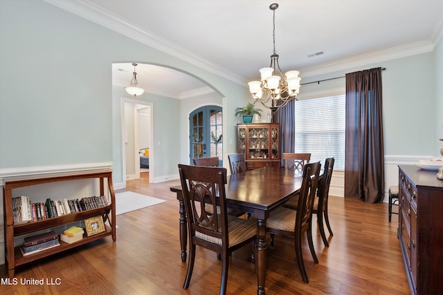 dining area with ornamental molding, arched walkways, baseboards, and wood finished floors