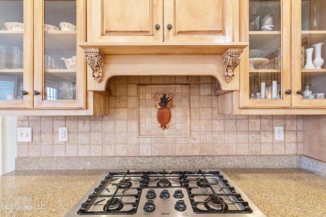 kitchen with stainless steel gas cooktop, light stone counters, backsplash, and glass insert cabinets