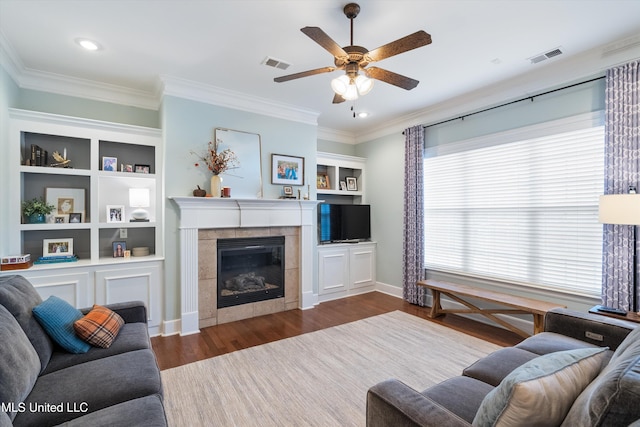 living room with a tiled fireplace, visible vents, crown molding, and wood finished floors