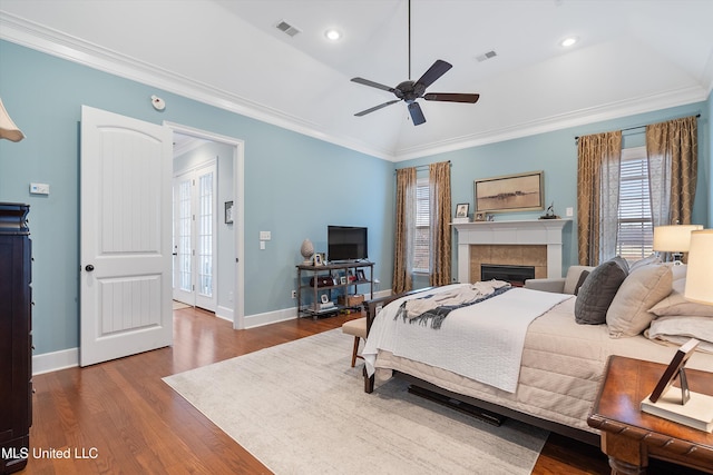 bedroom featuring a tiled fireplace, wood finished floors, visible vents, and crown molding