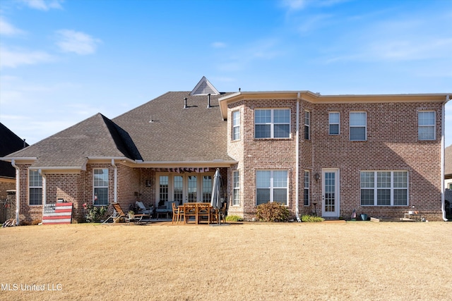 view of front of home featuring a patio, brick siding, roof with shingles, and a front yard