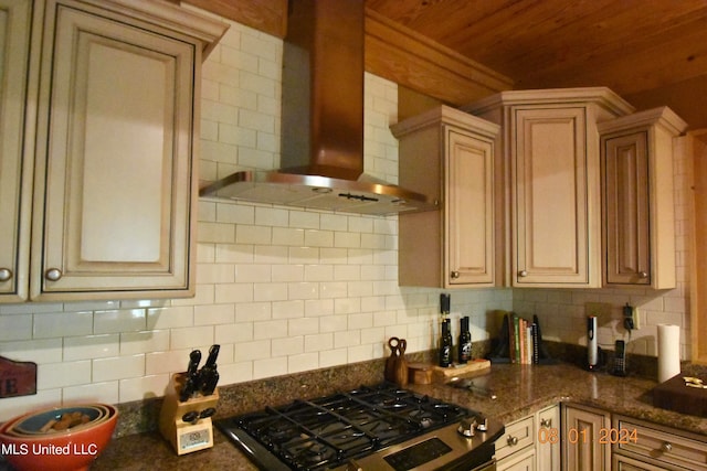 kitchen featuring black gas range, stovetop, wall chimney range hood, backsplash, and dark stone counters