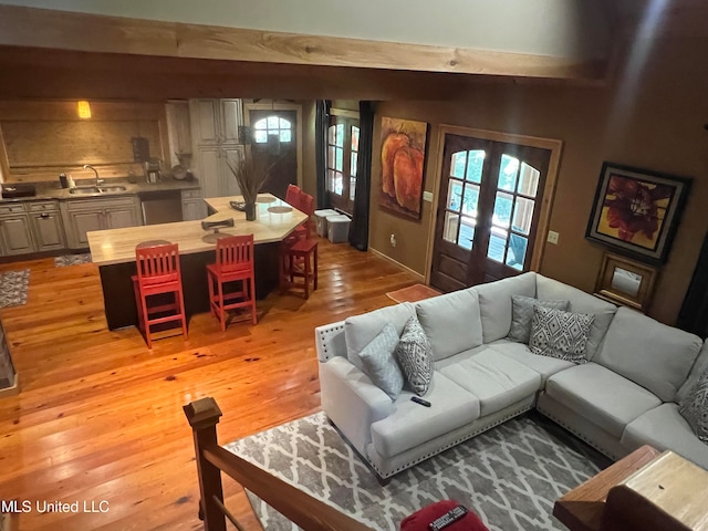 living room with light hardwood / wood-style floors, french doors, beam ceiling, and sink