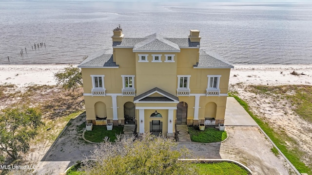 view of front facade featuring a shingled roof, a water view, and stucco siding