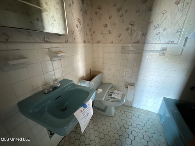 bathroom featuring a tub to relax in, tile patterned flooring, toilet, tile walls, and sink