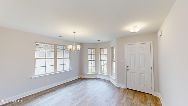 empty room with light hardwood / wood-style floors, a notable chandelier, and plenty of natural light