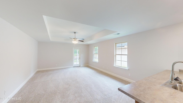 carpeted spare room with sink, a tray ceiling, plenty of natural light, and ceiling fan