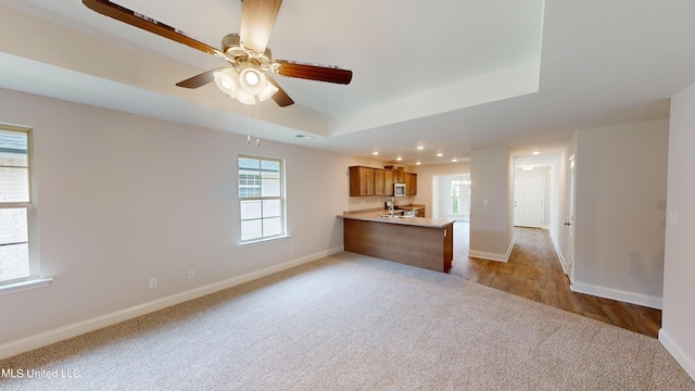 unfurnished living room with a tray ceiling, light wood-type flooring, and ceiling fan