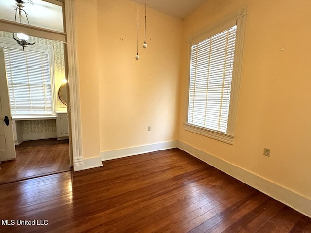 empty room with dark hardwood / wood-style floors, an inviting chandelier, and a healthy amount of sunlight