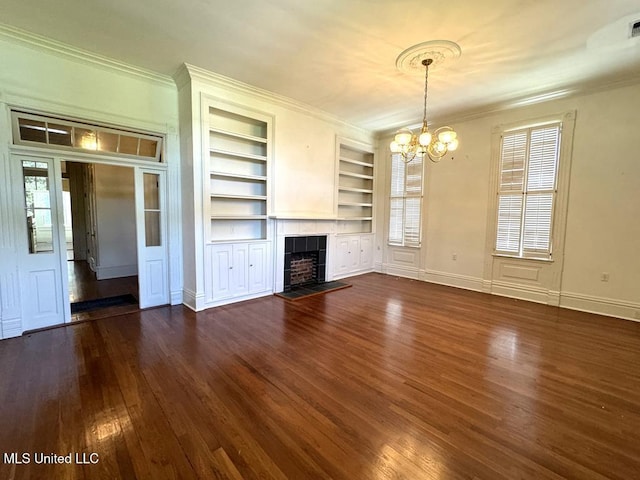 unfurnished living room featuring built in features, a chandelier, dark hardwood / wood-style floors, plenty of natural light, and a tiled fireplace