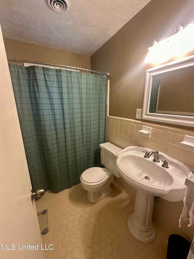 bathroom featuring a textured ceiling, tile walls, toilet, a shower with shower curtain, and tile patterned flooring