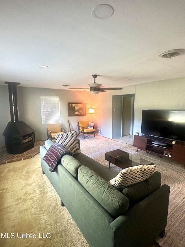 carpeted living room featuring ceiling fan and a wood stove