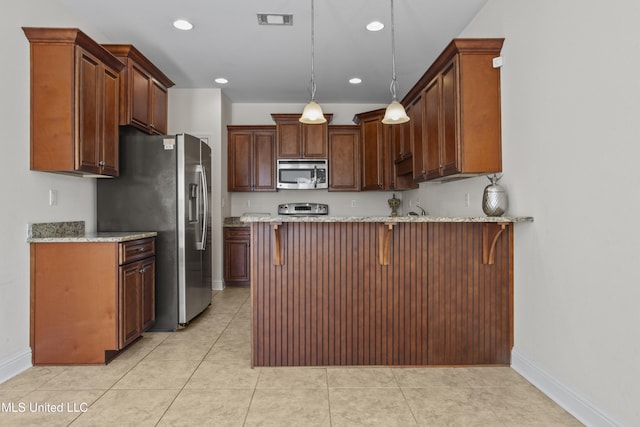 kitchen featuring hanging light fixtures, light stone countertops, appliances with stainless steel finishes, and a breakfast bar