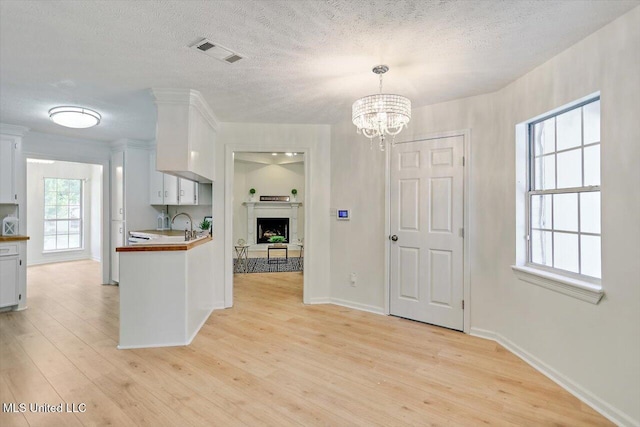 602 Hathaway Dr, Clinton, MS 39056 - kitchen with light wood-style floors, white cabinetry, a chandelier, a textured ceiling, and a fireplace with raised hearth