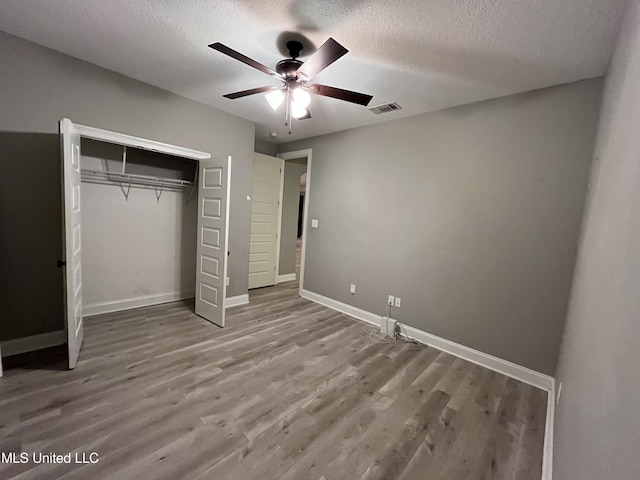 unfurnished bedroom featuring a closet, visible vents, a textured ceiling, and wood finished floors