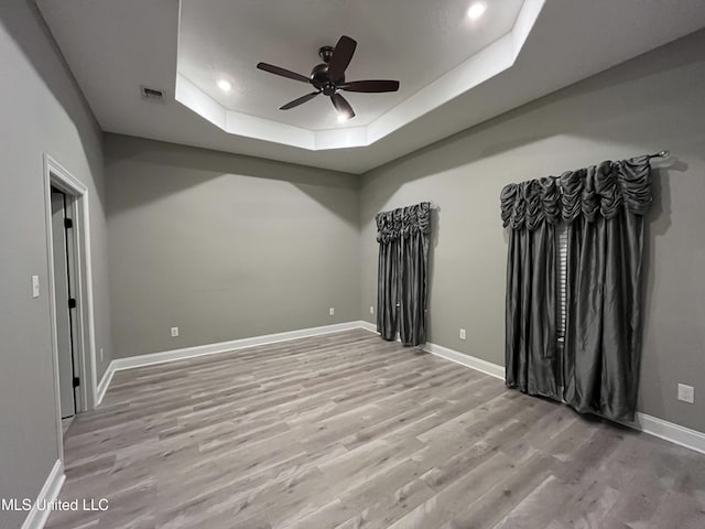 unfurnished room with wood finished floors, a ceiling fan, visible vents, baseboards, and a raised ceiling