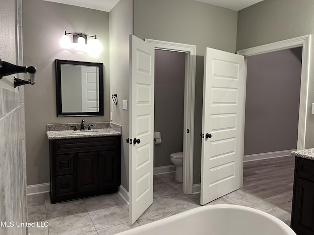 full bath featuring baseboards, a freestanding bath, vanity, and toilet