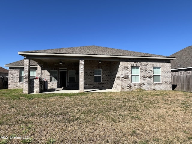 rear view of house with brick siding, a shingled roof, a lawn, a patio area, and fence