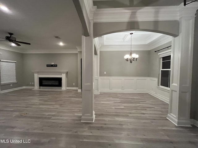 unfurnished dining area with ceiling fan with notable chandelier, a fireplace, wood finished floors, and crown molding