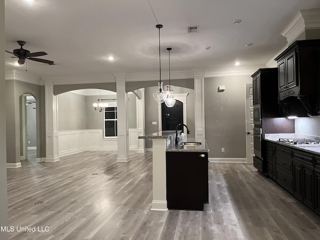 kitchen featuring arched walkways, stainless steel gas stovetop, wall oven, a sink, and dark cabinets