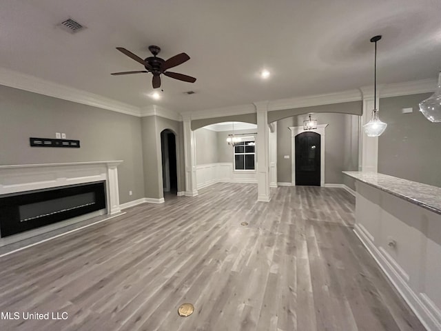 unfurnished living room with ornamental molding, arched walkways, a glass covered fireplace, and visible vents